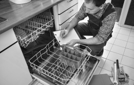 Male Technician Sitting Near Dishwasher Writing On Clipboard In Kitchen