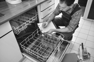 Male Technician Sitting Near Dishwasher Writing On Clipboard In Kitchen